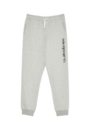 Junge mit lockigem Haar, der einen schwarzen und grauen Quiksilver Hoodie, graue Jogginghose und schwarze Sneakers trägt, steht mit einer Hand in der Tasche.