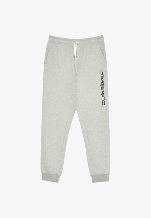 Junge mit lockigem Haar, der einen schwarzen und grauen Quiksilver Hoodie, graue Jogginghose und schwarze Sneakers trägt, steht mit einer Hand in der Tasche.