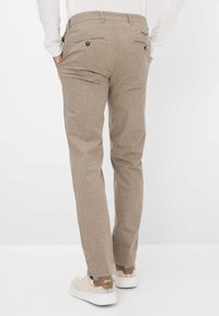 Beige geblokte broek met een slim fit, voorzien van twee achterzakken, knoopsluitingen en een subtiele textuur. Gecombineerd met lichtgekleurde sneakers.