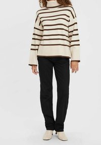 Pull crème à rayures horizontales marron, col montant, texture côtelée, associé à un pantalon noir à jambes droites et des bottines beige.
