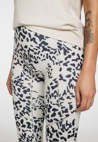 Leggings a vita alta di un leggero beige con stampa leopardata nera. Realizzati in tessuto elasticizzato con cuciture piatte e una vestibilità aderente.