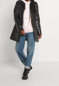 Černý lesklý trenčkot přes světle růžovou mikinu, v kombinaci se světlomodrými zkrácenými džínami a černými bojovými botami.