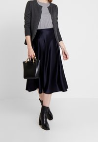Szary kardigan na szarym t-shircie, zestawiony z granatową satynową midi spódnicą. Czarna skórzana torebka ze złotymi okuciami i czarne botki za kostkę.