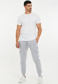 T-shirt blanche à col ras du cou associée à un pantalon de survêtement cargo gris clair avec poches latérales, poignets élastiques et accent de logo noir. Baskets blanches.