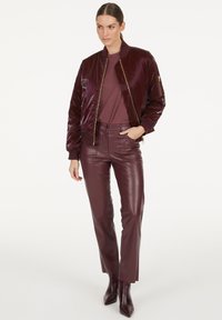 Burgunderfarbener Bomberjacke aus Satin mit gerippten Bündchen und Kragen, kombiniert mit passenden, schmal geschnittenen Lederhosen und Stiefeletten.
