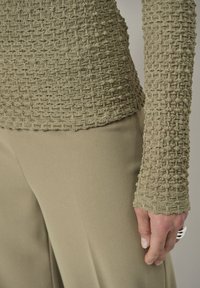 Olijfgroene gebreide top met textuur, met een aansluitende pasvorm en lange mouwen, gecombineerd met gladde, lichtgroene broeken met een subtiele glans.