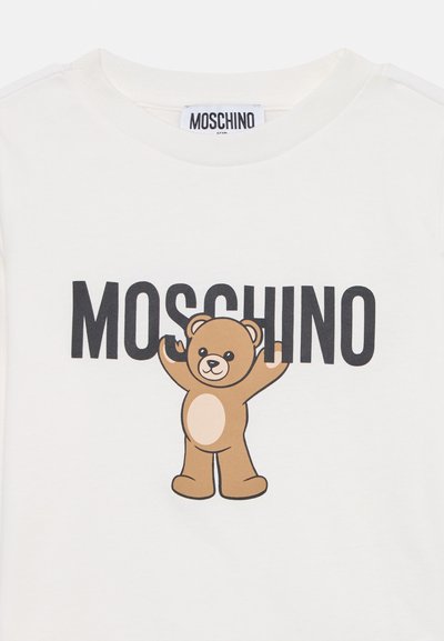 Fehér pamut póló nagy barna plüssmaci grafikával és mellette vastag "MOSCHINO" felirattal, fekete kiegészítőkkel. Kerek nyakkivágás.