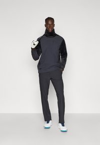 Outfit sportiv compus dintr-un top lung cu maneci de catifea neagră, de culoare gri închis, asortat cu pantaloni gri și pantofi de golf albi.