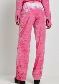 Rosa samtige weit geschnittene Hose mit strukturiertem Finish und glänzenden Akzenten. Verfügt über eine taillierte Taille und schwarze Knopfdetails auf der Rückseite.