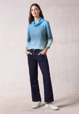 Blaues Gradient-Pullover mit Kragen und horizontalen Streifen, kombiniert mit dunkelblauen Hosen und weißen Sneakern. Glatte Textur und lässiges Design.