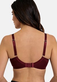 Marroninruskea rintaliivit säädettävillä olkaimilla ja hakaskiinnityksellä. Sisältää sileää satiinikangasta ja koristeelliset stingaukset reunoilla.