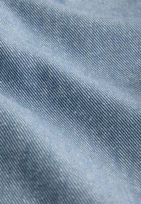 Gros plan sur un tissu en denim bleu clair montrant la texture en sergé diagonal et de légers plis.