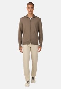 Pruun lukupeaga kardigan kergest kudumist, koos beežide pükstega. Sile tekstuur ja istuv disain. Minimalistlik stiil, ilma nähtavate mustriteta.