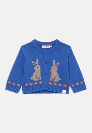 Blå strikket cardigan med to grå kaniner med oransje sløyfer, knappelukking og diamantmønster langs kanten. Merke: TINY.