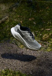 Baskets de course grises avec un dessus en maille, accents noirs et une semelle texturée. Présente un design épuré et un logo sur le côté.