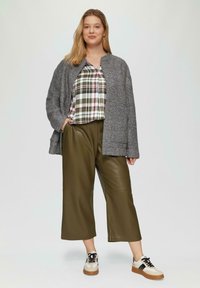 Grau melierte Jacke, grüne Kunstleder-Hose mit weiter Beinschnitt und ein kariertes Hemd in Rot, Weiß und Grün. Abgerundet mit beigen Sneakers.