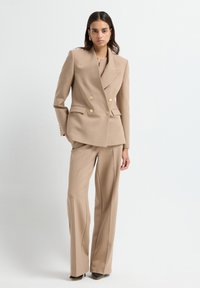 Beige Doppelreiher-Blazer mit zwei goldfarbenen Knöpfen, kombiniert mit passenden weit geschnittenen Hosen. Glattes Gewebe, taillierte Passform.