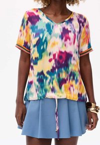 Top multicolore con scollo a V e maniche corte; presenta un dettaglio a fiocco nella parte inferiore. Abbinato a una gonna plissettata blu. Tessuto liscio e leggero.