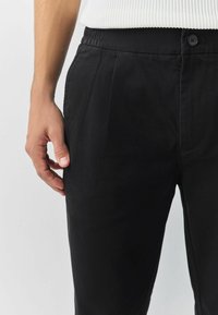 Black trousers with a straight cut, featuring a smooth fabric texture, elastic waist, and a button closure at the front.
