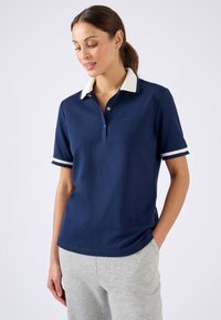 Polo bleu marine avec un col et des rayures de poignets de couleur claire, une patte de boutonnage à trois boutons et un petit logo sur la poitrine.