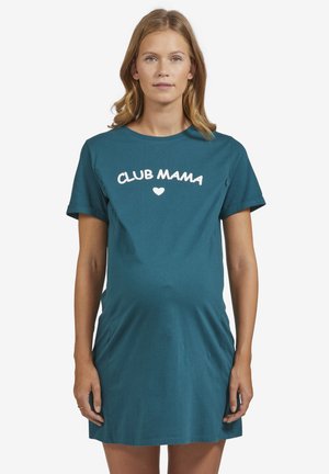 Schwangere Frau mit hellbraunen Haaren, die ein türkisfarbenes Kurzarmkleid mit der Aufschrift "CLUB MAMA" und einem Herz auf der Brust trägt.