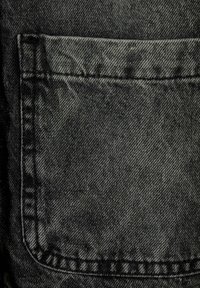 Tejido de mezclilla negra con un bolsillo trasero cuadrado con costuras visibles y un acabado texturizado, destacando la durabilidad del material.