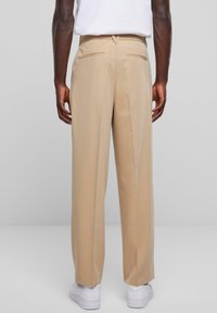 Beige, wijde broekspijpen met een vlakke voorkant, twee achterzakken en een gladde textuur. Draagt een fitted shirt met witte sneakers.