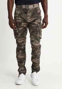 Camo cargo pants in groen- en bruintinten, met zijzakken en een taps toelopende pijp met een elastische manchette, gecombineerd met witte sneakers.