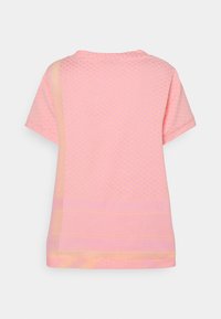 Camiseta de manga corta, de color rosa, con patrones texturizados, tela suave y un ajuste holgado. Incluye una banda horizontal en contraste.