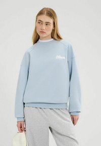 Sudadera azul clara con puños y bajo acanalados, que presenta un logo bordado en el frente. El material parece suave y texturizado.