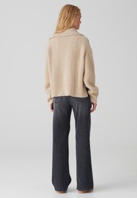 Maglione a costine beige con una vestibilità comoda e maniche larghe, abbinato a jeans svasati grigio scuro con dettagli di cucitura sottili.