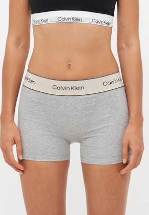 Gray cotton boxer briefs with a beige elastic waistband featuring the "Calvin Klein" logo in black. No patterns or additional accents.