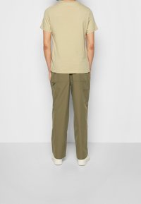 Krótka koszulka z krótkim rękawem w parze z oliwkowozielonymi spodniami typu cargo. Spodnie mają dwie przednie kieszenie i teksturowaną tkaninę. Casualowe obuwie jest białe.