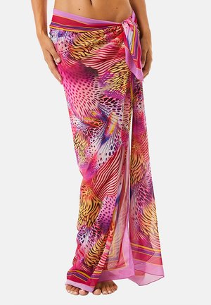 Sarong colorato e decorato con toni rosa, viola, giallo e rosso legato in vita, indossato sopra piedi nudi e addome scoperto.