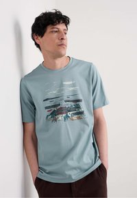 T-shirt azzurro chiaro a maniche corte in cotone, con un design grafico astratto multicolore che raffigura barche e nuvole.