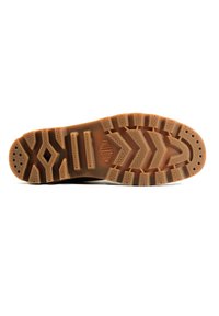 Semelle en caoutchouc brun avec un motif de grip texturé, présentant des crampons profonds, des rainures horizontales et diagonales, ainsi que de petits trous de drainage.