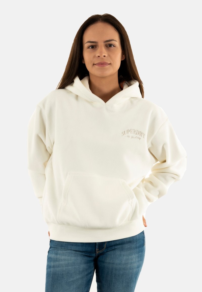 Haut à capuche blanc côtelé avec une poche kangourou et un logo. Dispose d'une capuche avec cordon de serrage et d'une coupe décontractée. Associé avec un jean bleu.