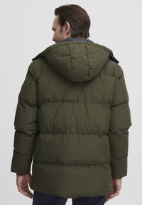 Olivgrön puffjacka med huva, har horisontell quiltning, dragkedjeslutning och ett slätt, mjukt yttertyg.