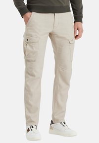 Pantalones cargo beige con dos bolsillos laterales, corte recto, detalles de costura y una textura suave. Combinado con zapatillas blancas.