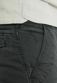 Dunkelgraue Baumwollhosen mit schräger Taschennaht, ausgestattet mit einem gestickten Logo auf der Gesäßtasche. Glatte Textur, taillierte Passform.