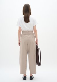 Beige high-waisted wide-leg trousers with a smooth texture, paired with a white short-sleeve t-shirt, and black shoes. Brown bag in hand.