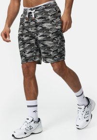 Bermudas de camuflaje en gris y negro, con cinturilla elástica y cordón, bolsillos laterales y un bolsillo tipo cargo para almacenamiento.