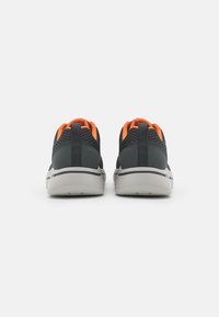 Scarpe sportive con tomaia in rete grigio scuro, dettagli arancioni e suola bianca. Presentano un colletto imbottito e linguette sul retro per facilitarne l'indossamento.