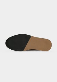 Semelle d'une chaussure habillée avec un grip en caoutchouc noir à l'avant et du cuir lisse couleur marron clair au talon et au milieu du pied.