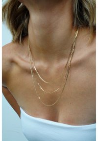 Goldfarbene Kettenhalskette mit verschiedenen Längen und Mustern, die eine glatte und reflektierende Textur auf nackter Haut aufweist.