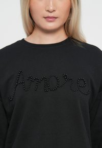 Felpa nera con la scritta "Amore" impreziosita da piccole perline nere. Collo rotondo e maniche lunghe, realizzata in un morbido tessuto testurizzato.