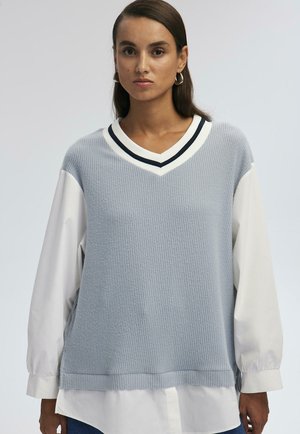 Light blue knitted sweater with a V-neck, featuring black and white trim, paired with a white long-sleeve shirt underneath.