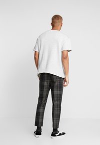 Lys grå t-shirt med oprullede ærmer, parret med sorte og grå ternede bukser. Modellen står med ryggen til, hvilket viser det afslappede fit og den uformelle stil.