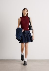 Haut sans manches bordeaux avec une fermeture éclair, jupe en jean noir en A, sac à main noir et chaussures noires avec des chaussettes blanches. Textures lisses et design ajusté.