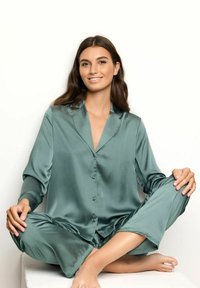 Satin pyjamastel in het groen, bestaande uit een geknoopte top met kraag en bijpassende broek. Gladde textuur, comfortabele pasvorm en broek tot de enkels.